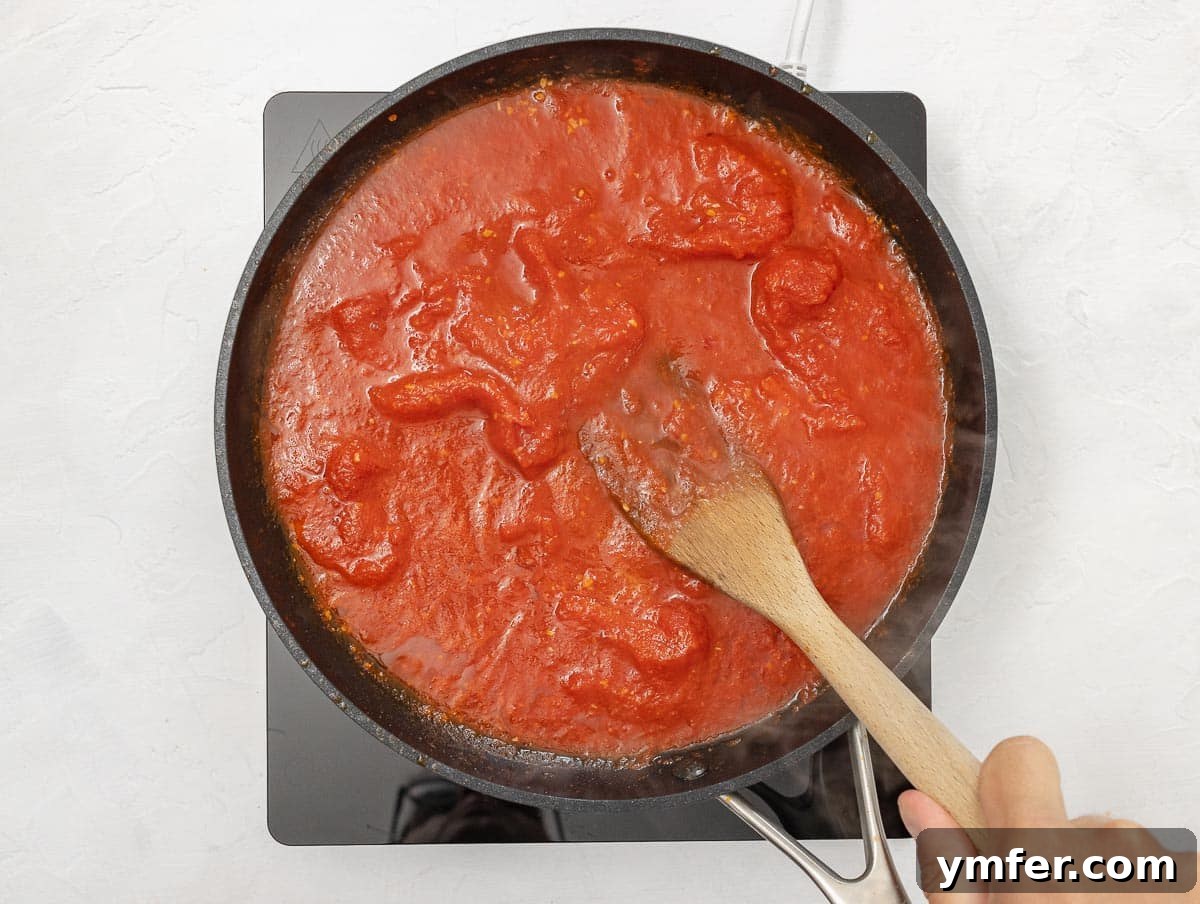 Fiery Rigatoni 7 crushing whole peeled tomatoes with a fork in a pan to make arrabbiata sauce