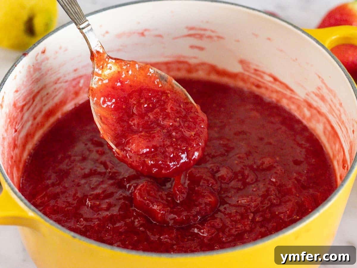 Summer in a Jar 3 Freshly cooked strawberry jam cooling in a medium-sized pot with a spoon resting on the side.