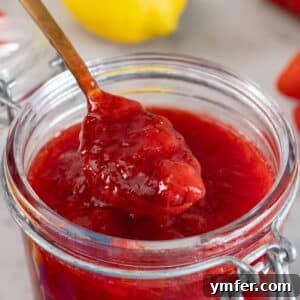 A teaspoon of vibrant homemade strawberry jam scooped from a glass jar.