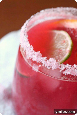 A beautifully crafted Blood Orange Margarita in a salt-rimmed glass, garnished with a vibrant blood orange wheel and a lime wedge, resting on a coaster.