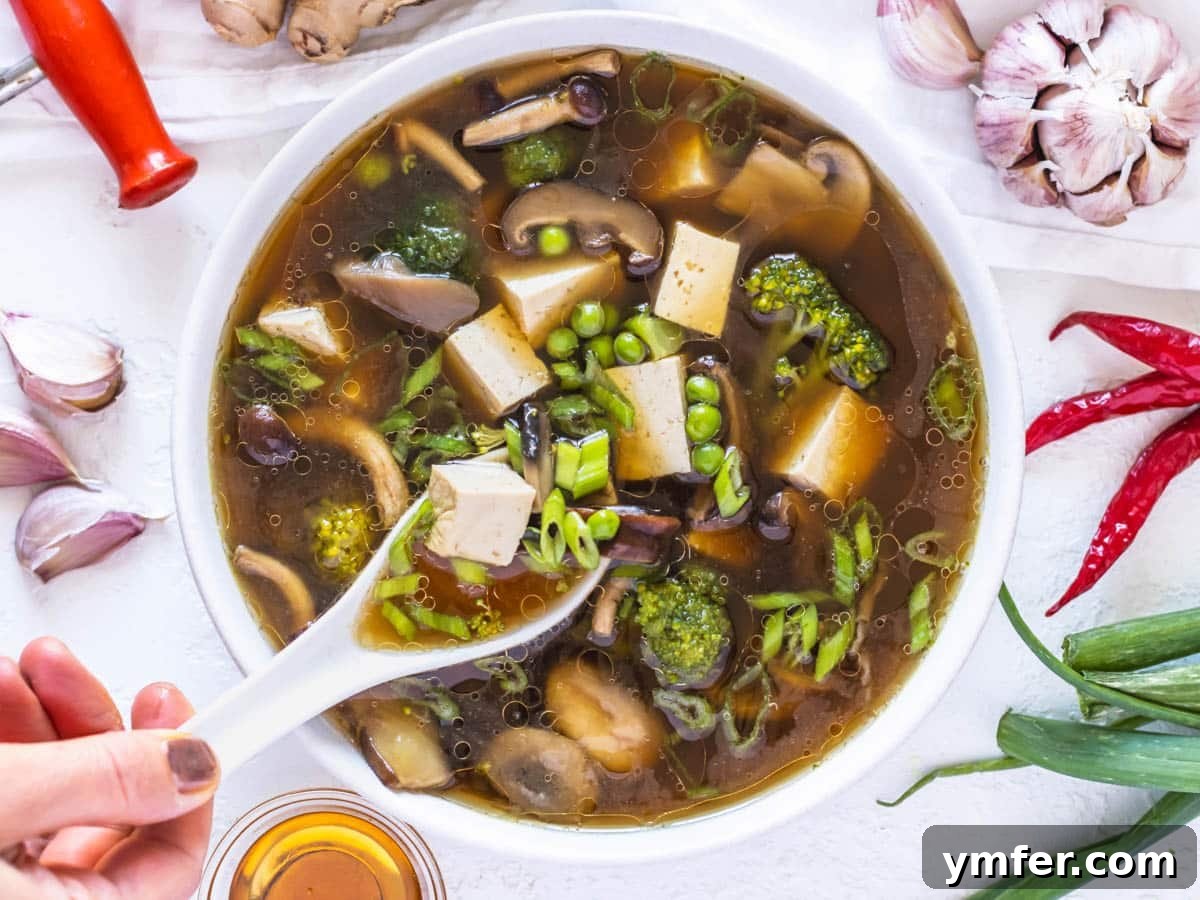 Feast on Plants: 35 Vibrant Recipes 23 Tofu soup recipe with a hand holding a white spoon, ready to serve.
