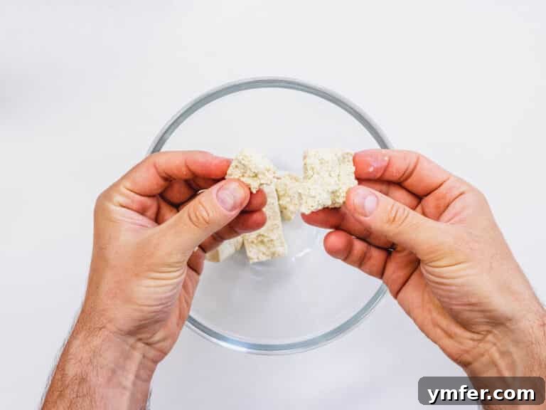 Tearing the tofu apart with hands for an uneven texture.