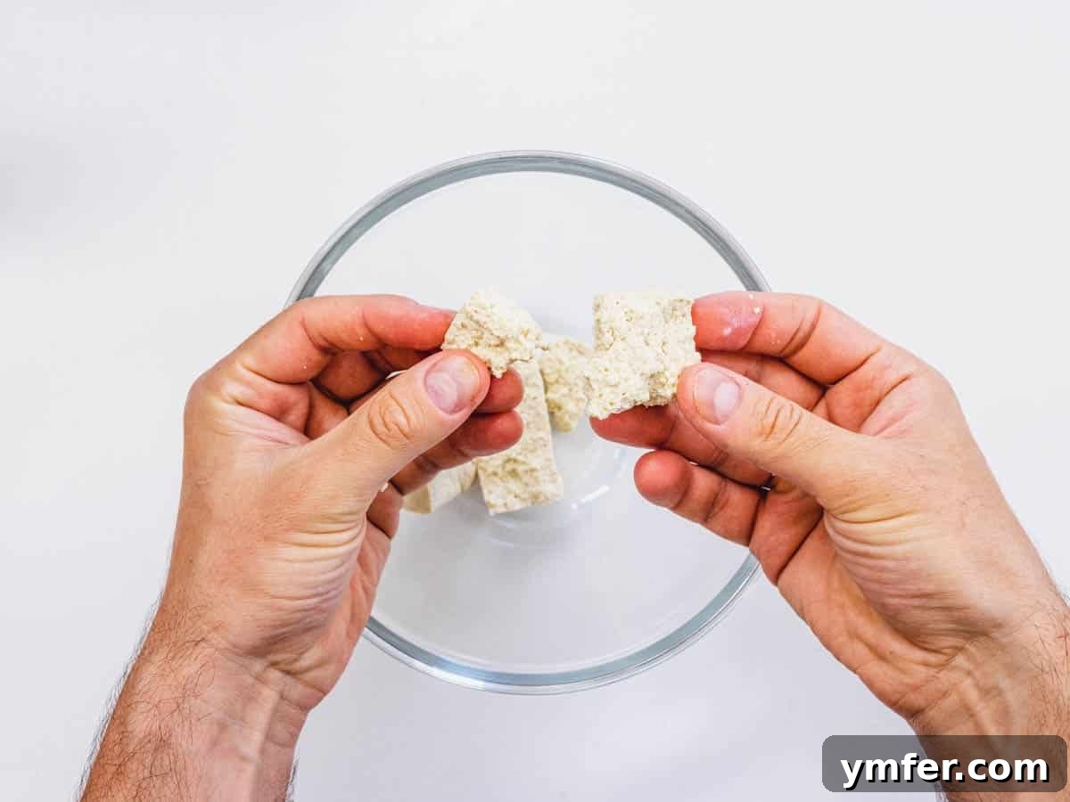Effortless Crispy Air Fryer Tofu 5 Tearing firm tofu apart with hands into rugged, bite-sized pieces.