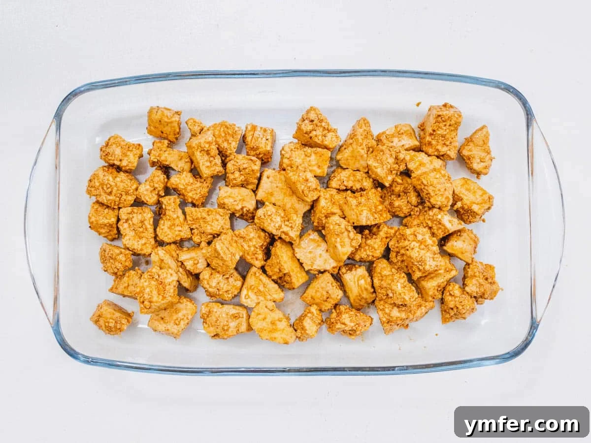 Effortless Crispy Air Fryer Tofu 6 Tofu pieces mixed with oil, soy sauce, and various spices in a bowl.