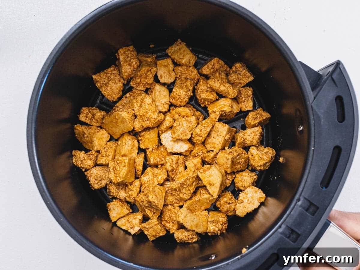 Effortless Crispy Air Fryer Tofu 7 Seasoned tofu pieces arranged in an air fryer basket before cooking.