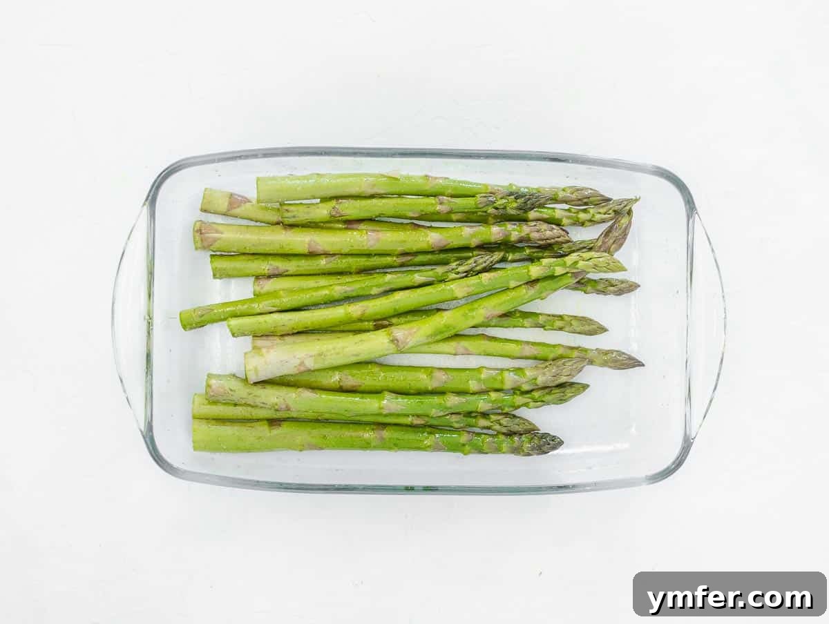Seasoning asparagus spears with olive oil, salt, and pepper in a bowl