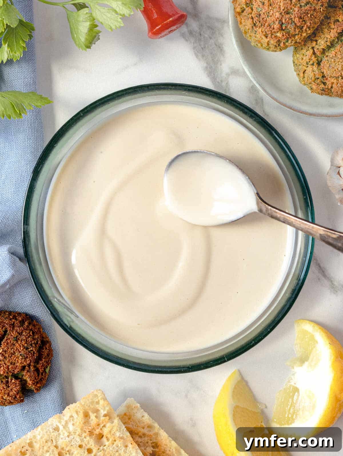Silky Tahini Drizzle 6 A glass bowl of creamy tahini sauce, garnished with lemon wedges, indicating readiness for serving.