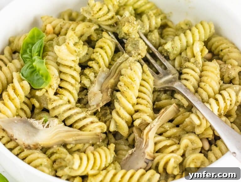 Artichoke pesto being mixed with pasta in a bowl with pasta water