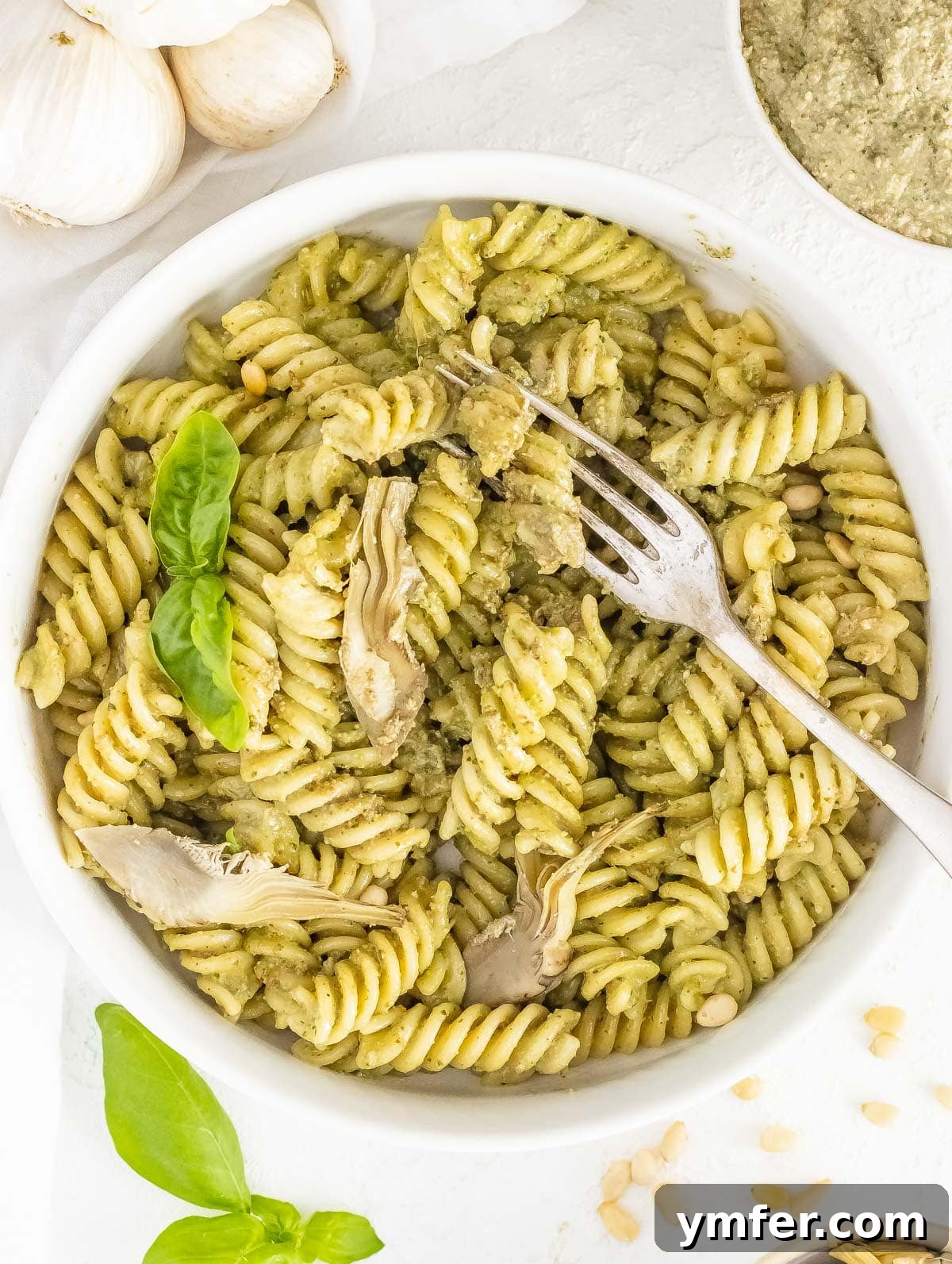 Savory Artichoke Spread 5 Artichoke pesto generously tossed with spaghetti pasta in a bowl, garnished with fresh basil leaves and a slice of lemon