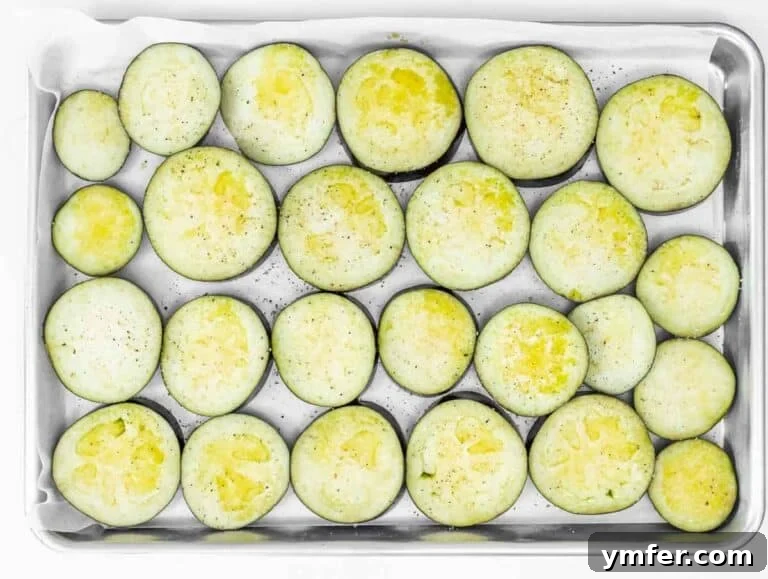 Eggplant Elevated 30 Exciting Recipes 26 Eggplant slices meticulously arranged on a baking tray with parchment paper, brushed with oil and seasoned.