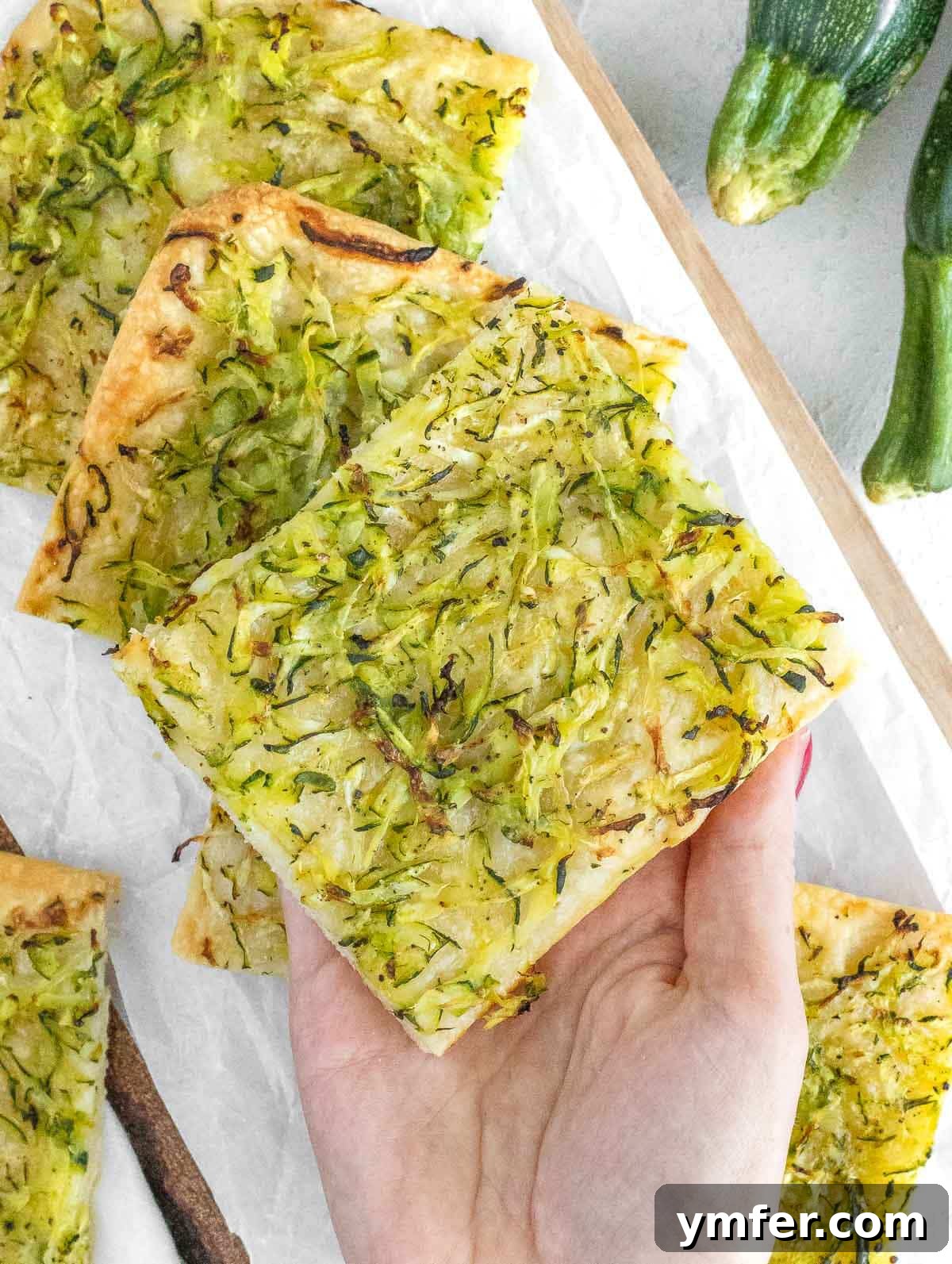 Rustic Zucchini Focaccia 4 A person holding a large slice of freshly baked zucchini focaccia, showing the delicious crust.
