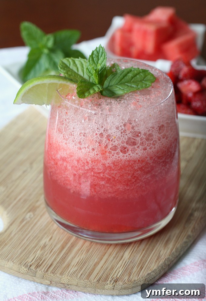Strawberry Watermelon Agua Fresca by Nutmeg Nanny A tall glass of vibrant red strawberry watermelon agua fresca, garnished with fresh mint and a lime wedge, sits on a wooden surface, embodying the perfect non-alcoholic summer treat.