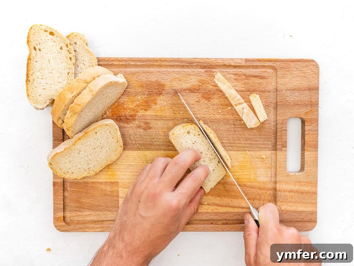 Golden Crunch Air Fryer Croutons 5 slicing off the crust of the bread. A hand using a serrated knife to remove the crust from a slice of bread.