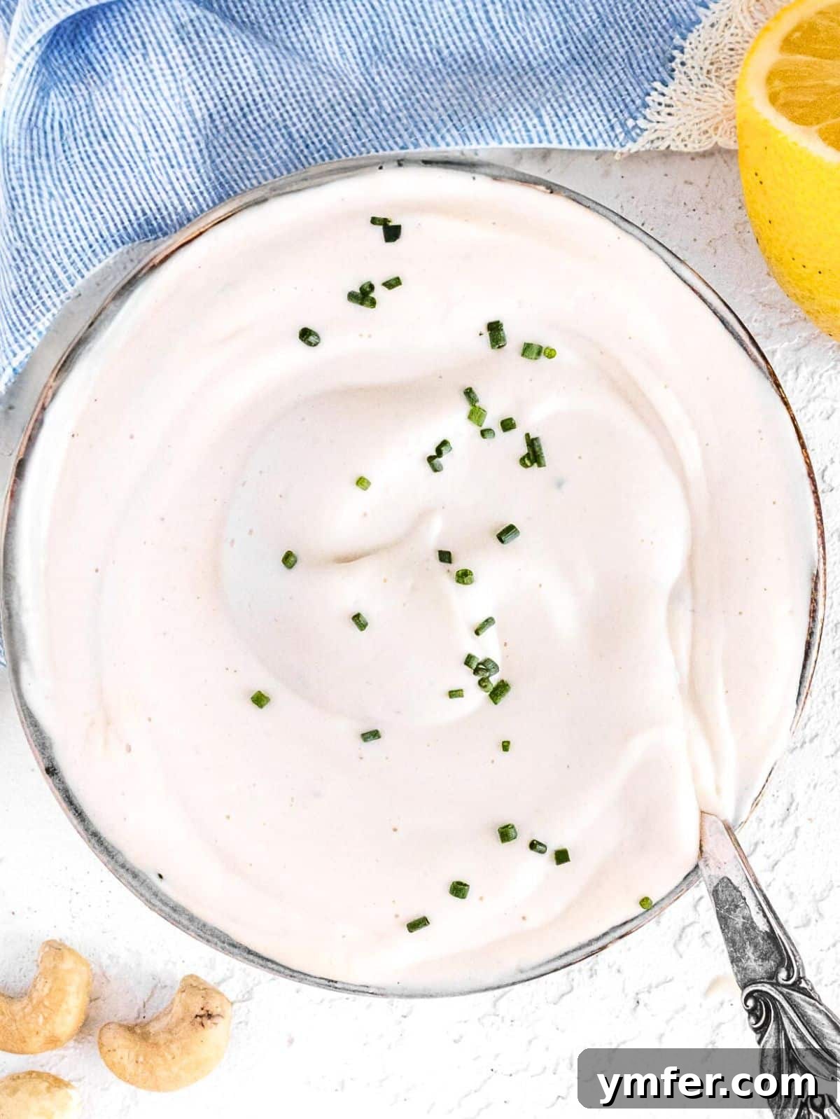 Velvety Vegan Sour Cream 2 Vegan sour cream with cashews and a silver spoon, showcasing its creamy texture.
