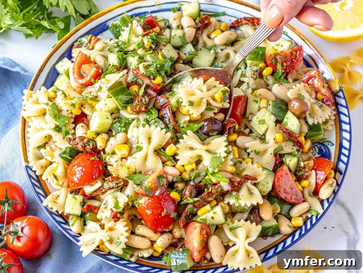 35 Vibrant Vegetarian Lunch Ideas 9 A colorful vegan pasta salad on a blue plate, with a hand holding a silver spoon.