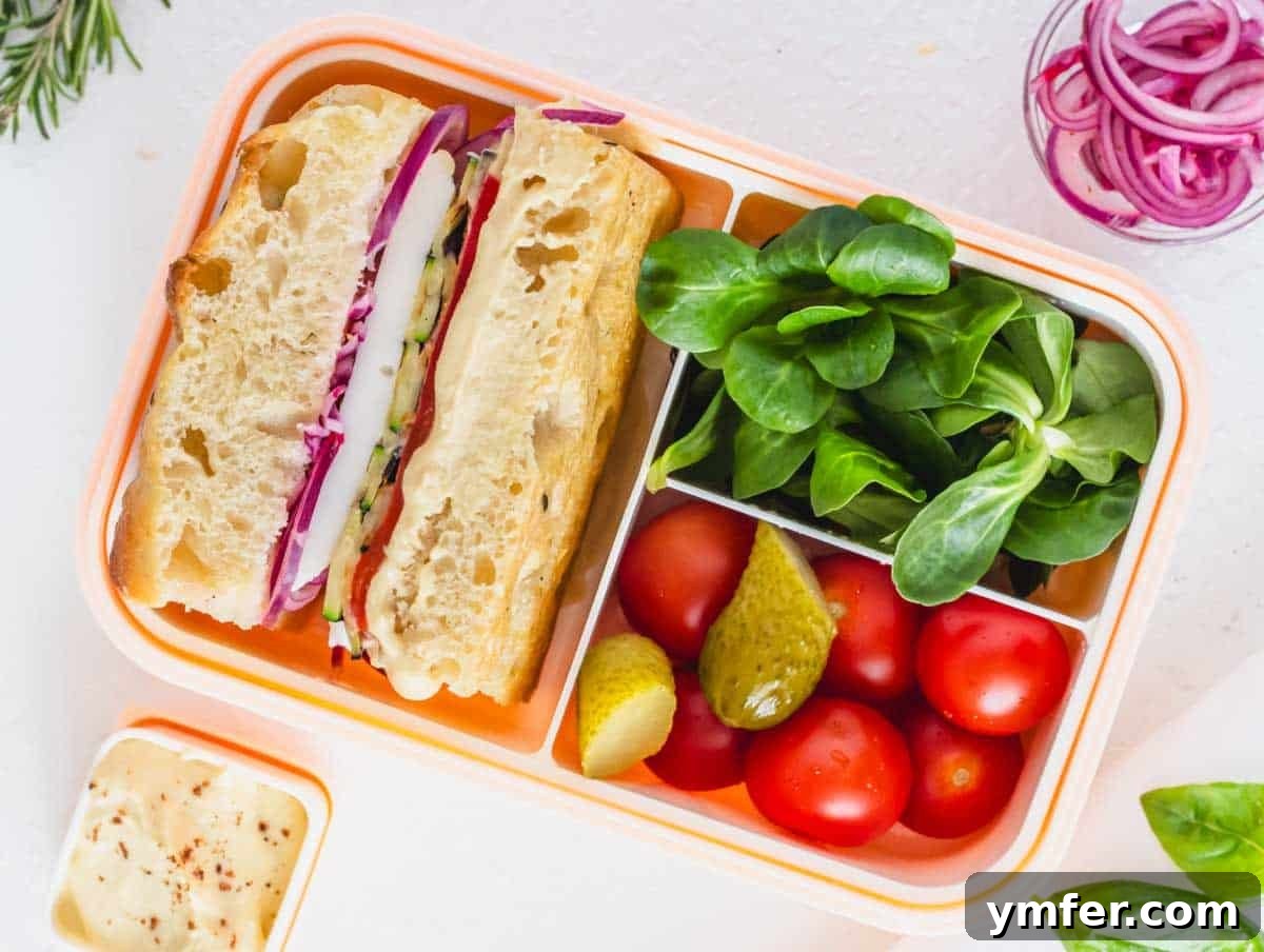 35 Vibrant Vegetarian Lunch Ideas 15 A gourmet focaccia sandwich packed in a pink bento box with fresh vegetables.