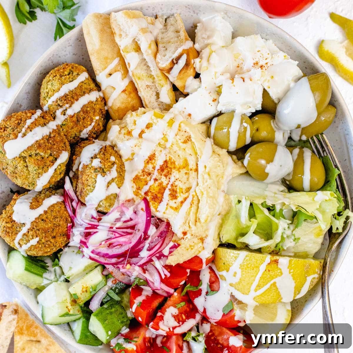 Mediterranean hummus bowl with fresh vegetables, olives, and pita.