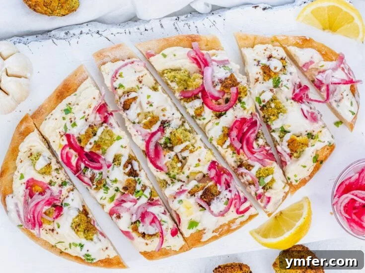 Flatbread pizza topped with hummus, falafel, and pickled onions.