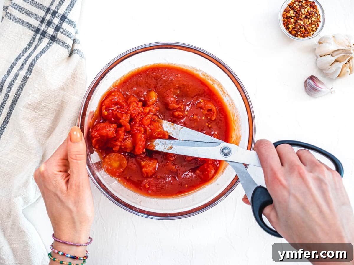 Rustic Marinara 7 hand using scissors to cut whole peeled tomatoes