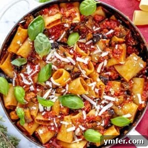 Pasta alla Norma served in a skillet with fresh basil and oregano.