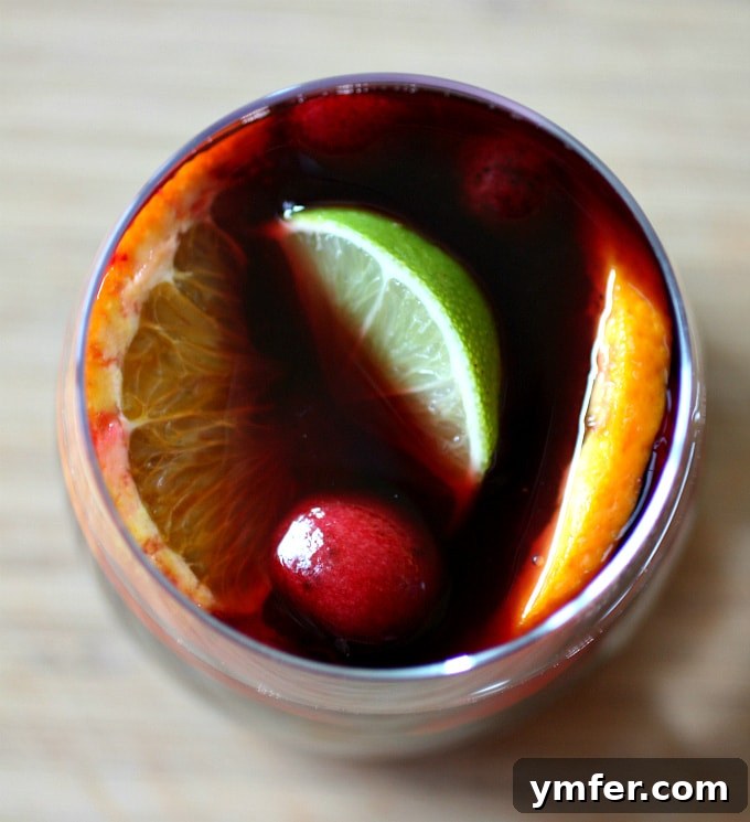 A large pitcher of vibrant red wine sangria, filled with sliced oranges, limes, apples, strawberries, and cherries, ready to be served on a sunny summer day.