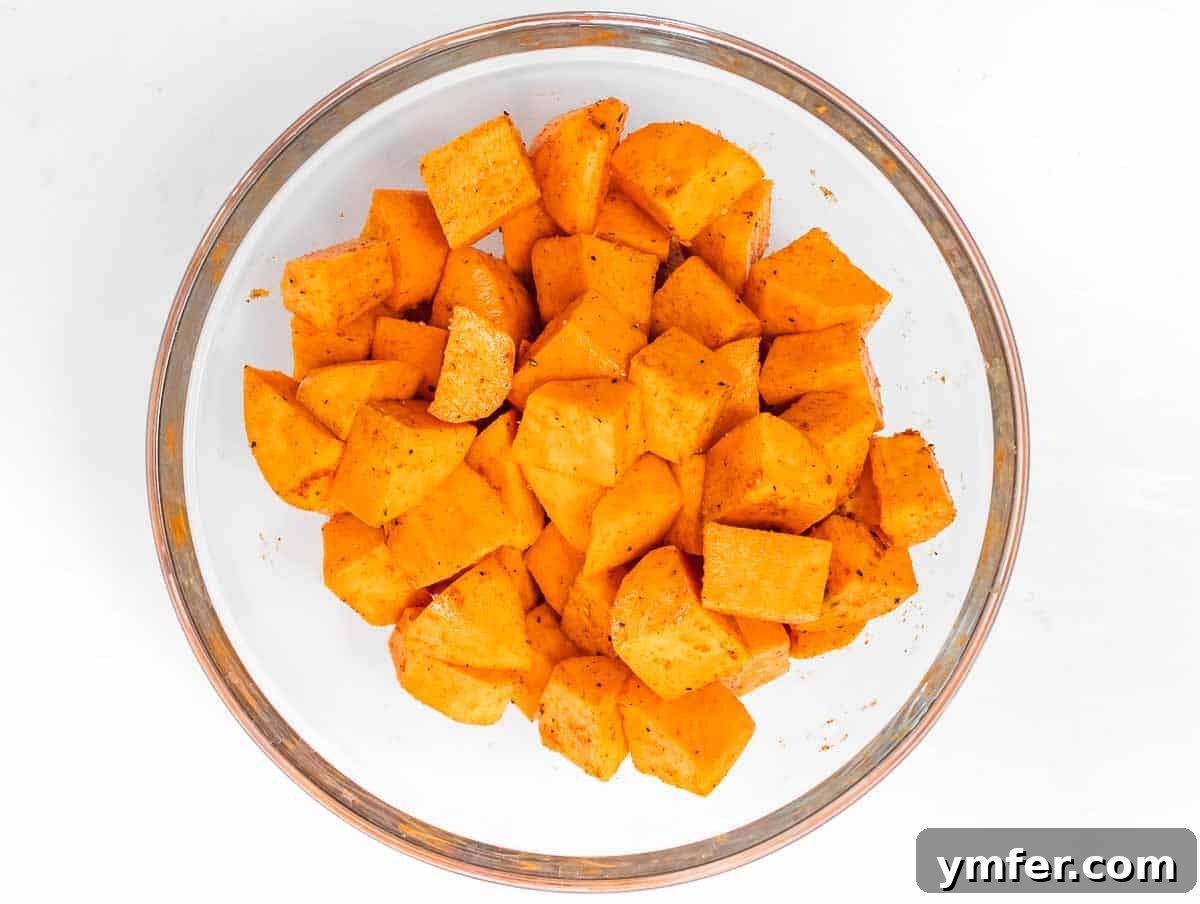 Golden & Crispy Air Fryer Sweet Potatoes 6 Sweet potato cubes being tossed with olive oil and a blend of spices in a mixing bowl.