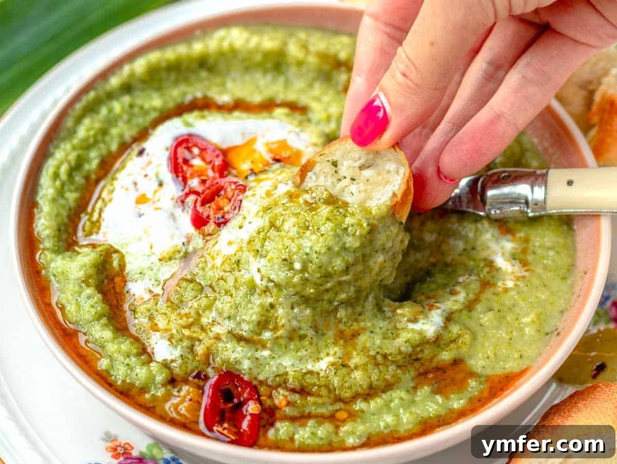 Vibrant Broccoli Cream 4 Hand holding a piece of crusty garlic bread, dipping it into a bowl of creamy broccoli soup, emphasizing the interactive and comforting aspect of the meal.