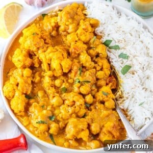 Cauliflower curry with rice and a spoon, garnished with fresh herbs.