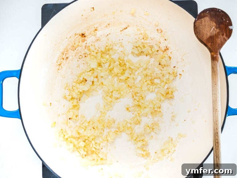 Onions, garlic, and ginger sautéing in olive oil in a blue skillet.