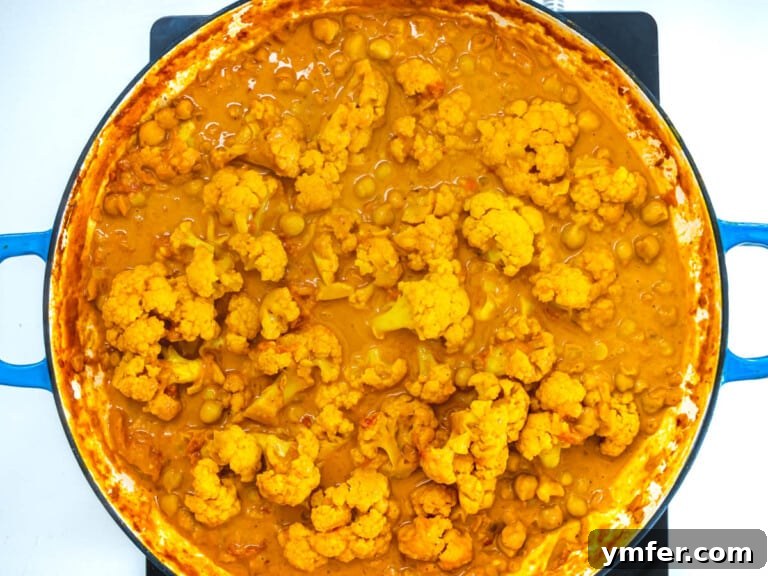 The finished cauliflower curry resting in a blue skillet after cooking.