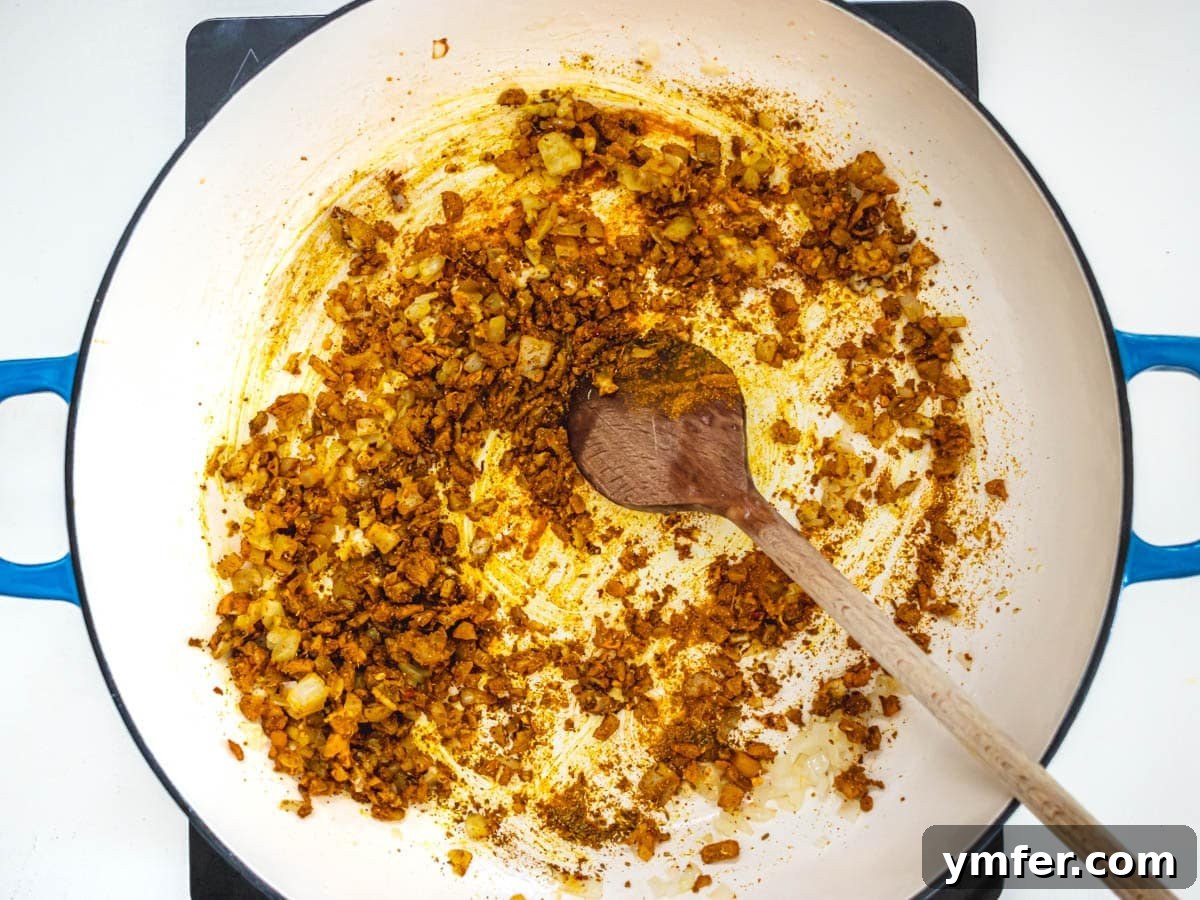 Golden Cauliflower Curry 4 Sautéing onions, garlic, and ginger in a blue skillet, creating the aromatic foundation for the curry.