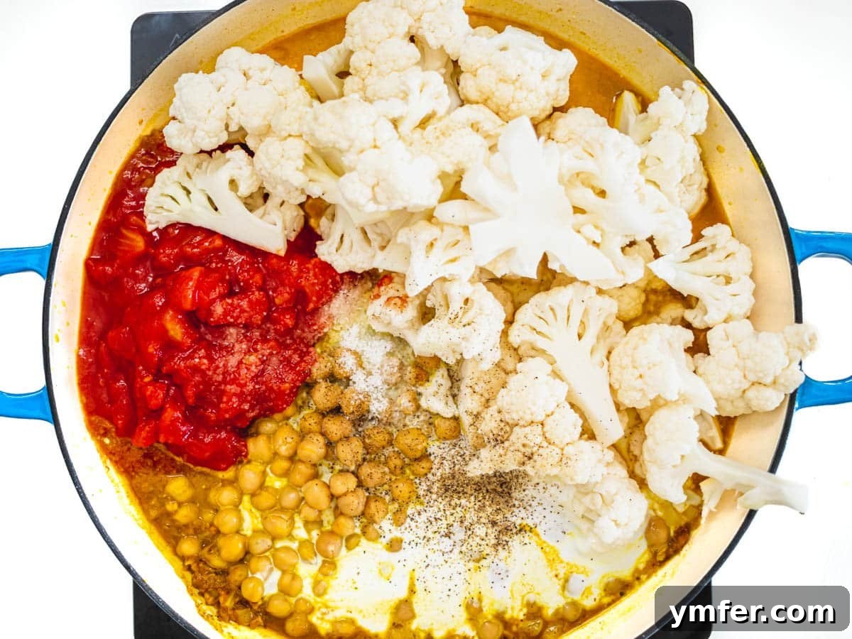 Golden Cauliflower Curry 5 Canned tomatoes, chickpeas, and cauliflower simmering in a skillet with spices and coconut milk.