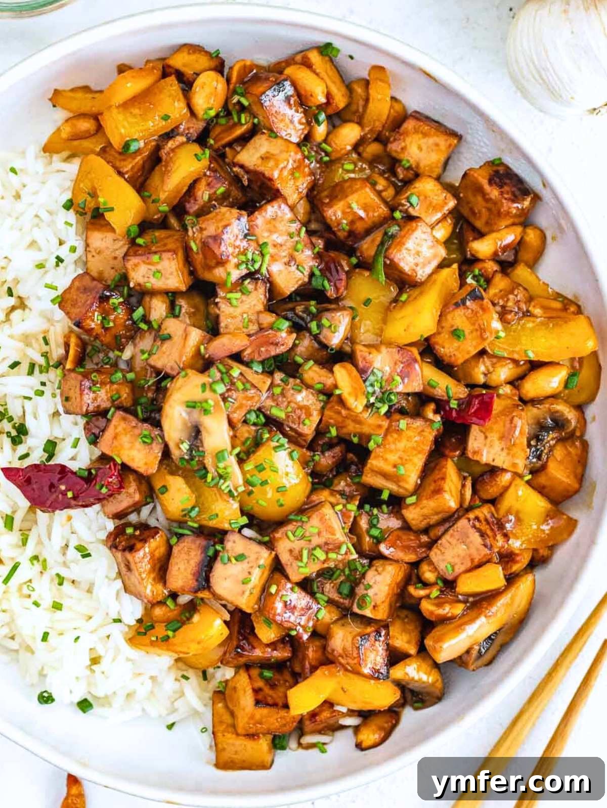 Kung Pao Tofu 2 Kung pao tofu with white rice and chopsticks, garnished with fresh herbs.