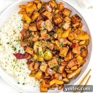 Kung pao tofu with rice in a white bowl, garnished with fresh herbs.
