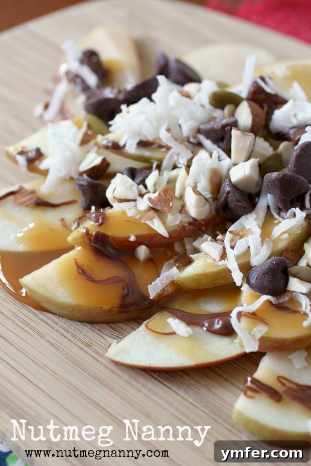 Apple Nachos by Nutmeg Nanny apple nachos on a wooden plate topped with nuts, coconut and chocolate.