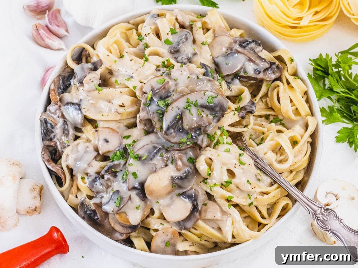 40 Flavorful Plant-Based Dinners 15 Creamy Mushroom Alfredo pasta, adorned with fresh parsley and a fork ready to twirl.