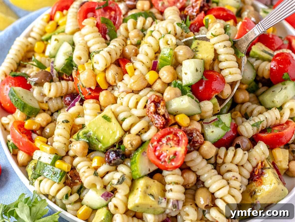 40 Flavorful Plant-Based Dinners 18 Refreshing chickpea pasta salad with avocado cubes, and a silver spoon ready for a bite.