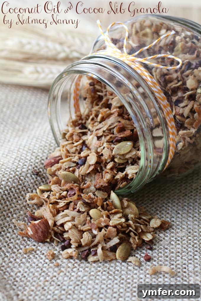 Homemade Coconut Oil & Cocoa Nib Granola A bowl of fresh, homemade coconut oil and cocoa nib granola, perfectly golden brown with visible oats, coconut flakes, chopped almonds, and dark cocoa nibs. It's ready to be served over yogurt or enjoyed as a snack.