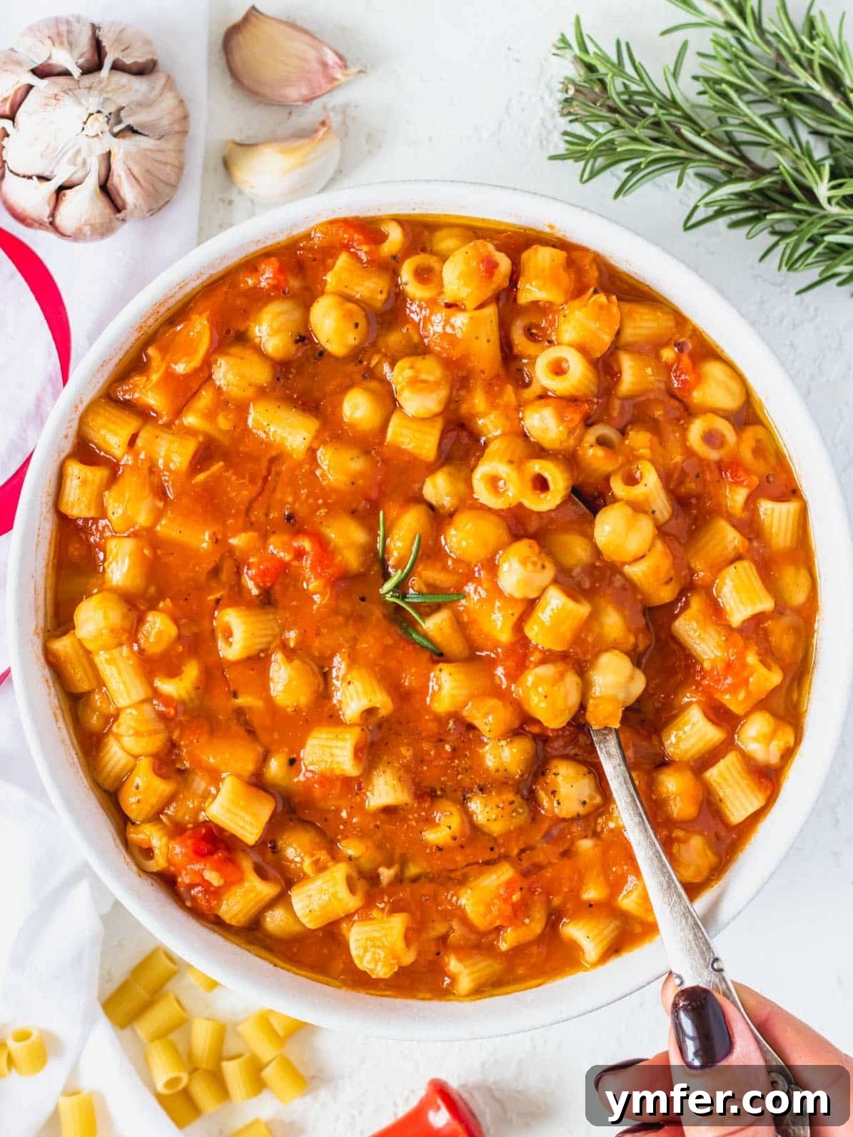 Hearty Chickpea Pasta 2 A bowl of creamy Pasta e Ceci with a hand holding a spoon, ready to be enjoyed.