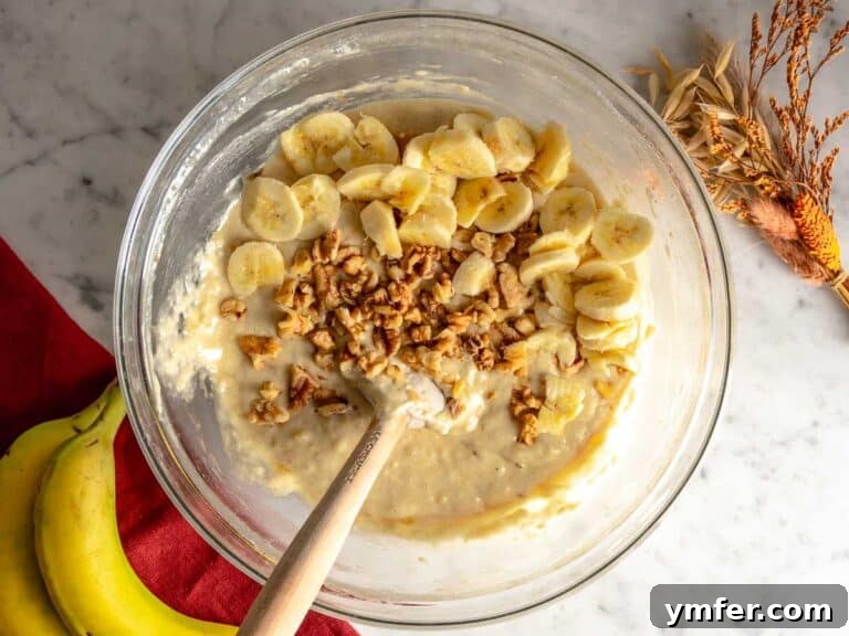 Batter in a glass bowl with walnuts and banana.
