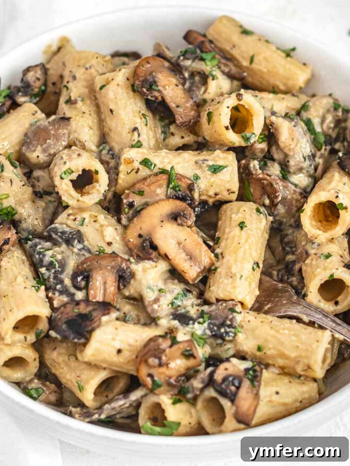 Creamy hummus pasta with mushrooms in a bowl, garnished with fresh parsley.