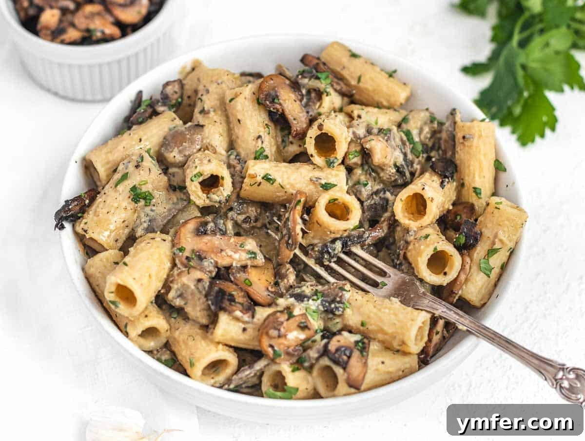 A forkful of hummus pasta with mushrooms and a sprinkle of parsley.