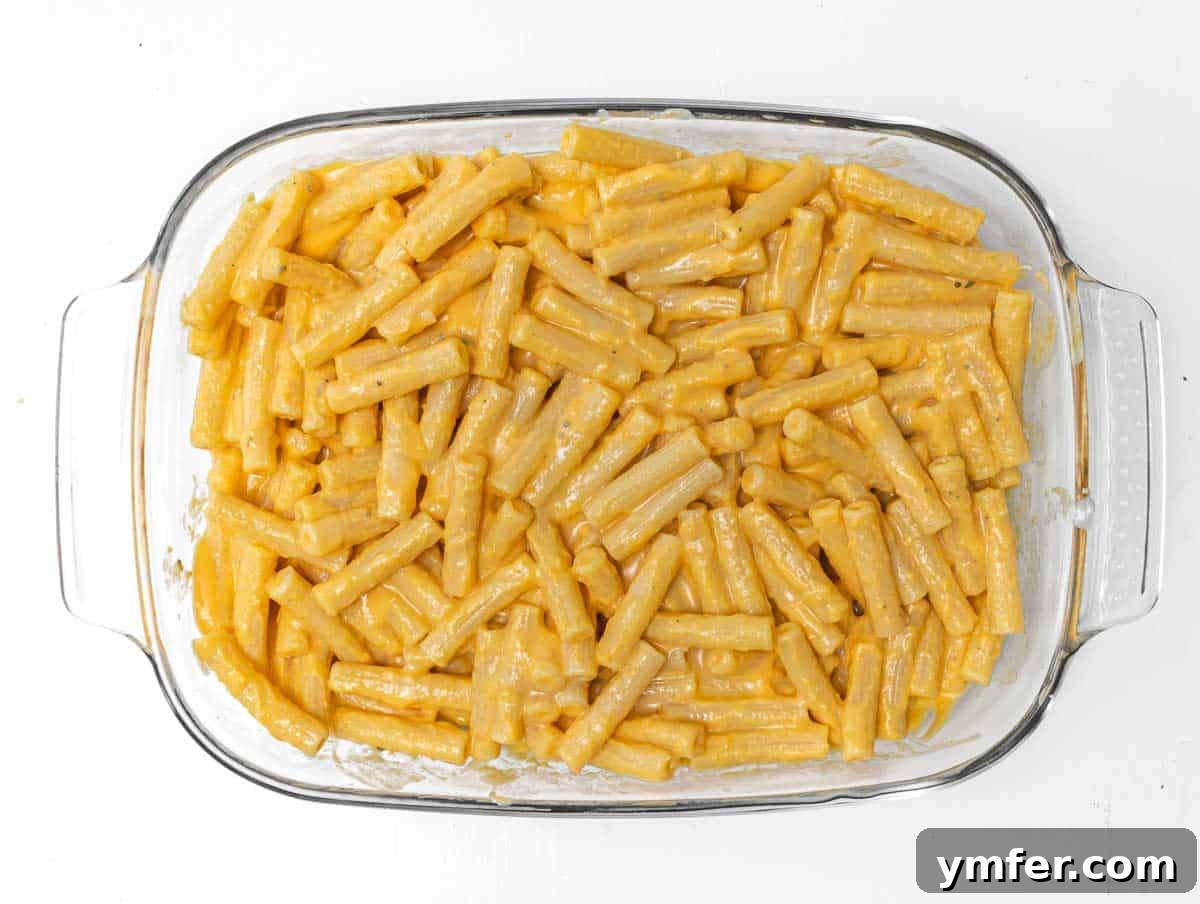 Golden Harvest Pumpkin Pasta 12 The pumpkin-coated pasta evenly distributed in a baking pan, ready for the final toppings.