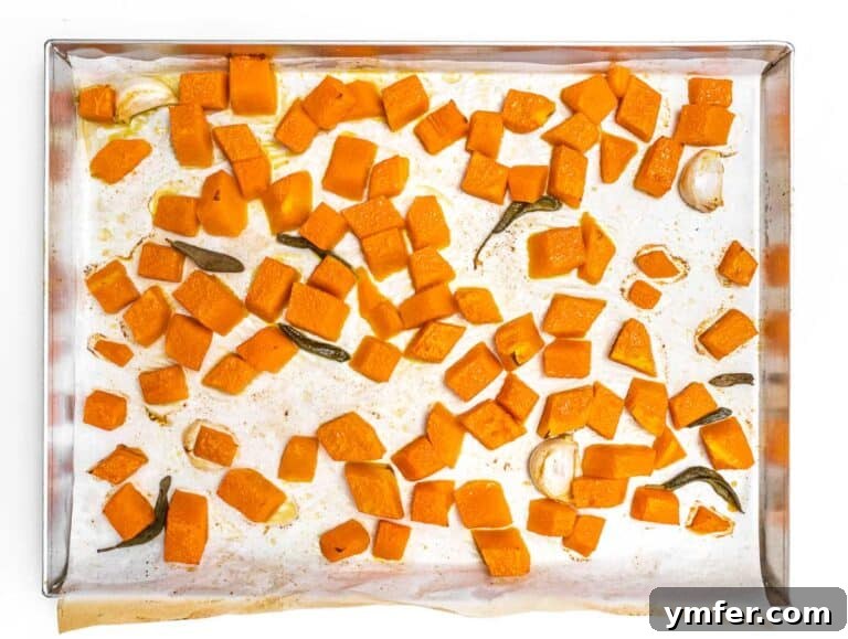 Golden Harvest Pumpkin Pasta 18 Roasted pumpkin pieces and sage leaves evenly spread on a parchment-lined baking tray.
