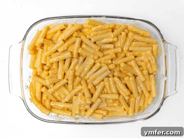 Golden Harvest Pumpkin Pasta 23 Pumpkin-coated pasta being transferred into a baking pan.
