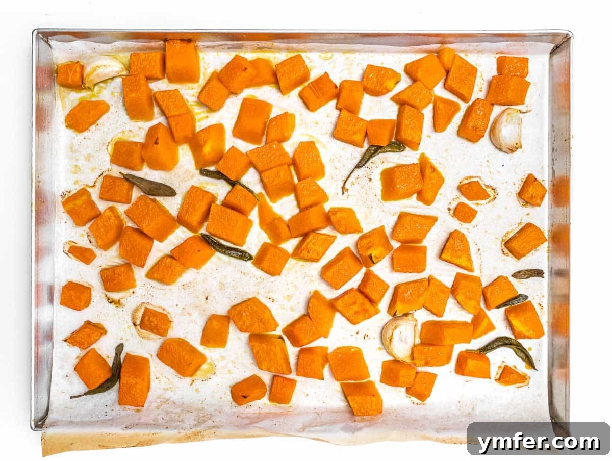 Golden Harvest Pumpkin Pasta 6 Close-up of diced pumpkin and sage leaves seasoned and spread on a baking tray, ready for roasting.