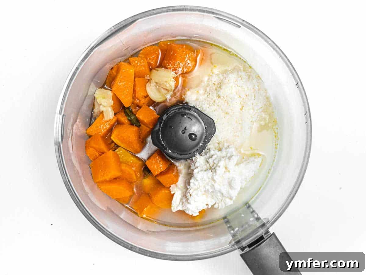 Golden Harvest Pumpkin Pasta 8 A food processor bowl filled with roasted pumpkin, peeled garlic, sage, ricotta, parmesan, and olive oil, ready to be blended into a sauce.