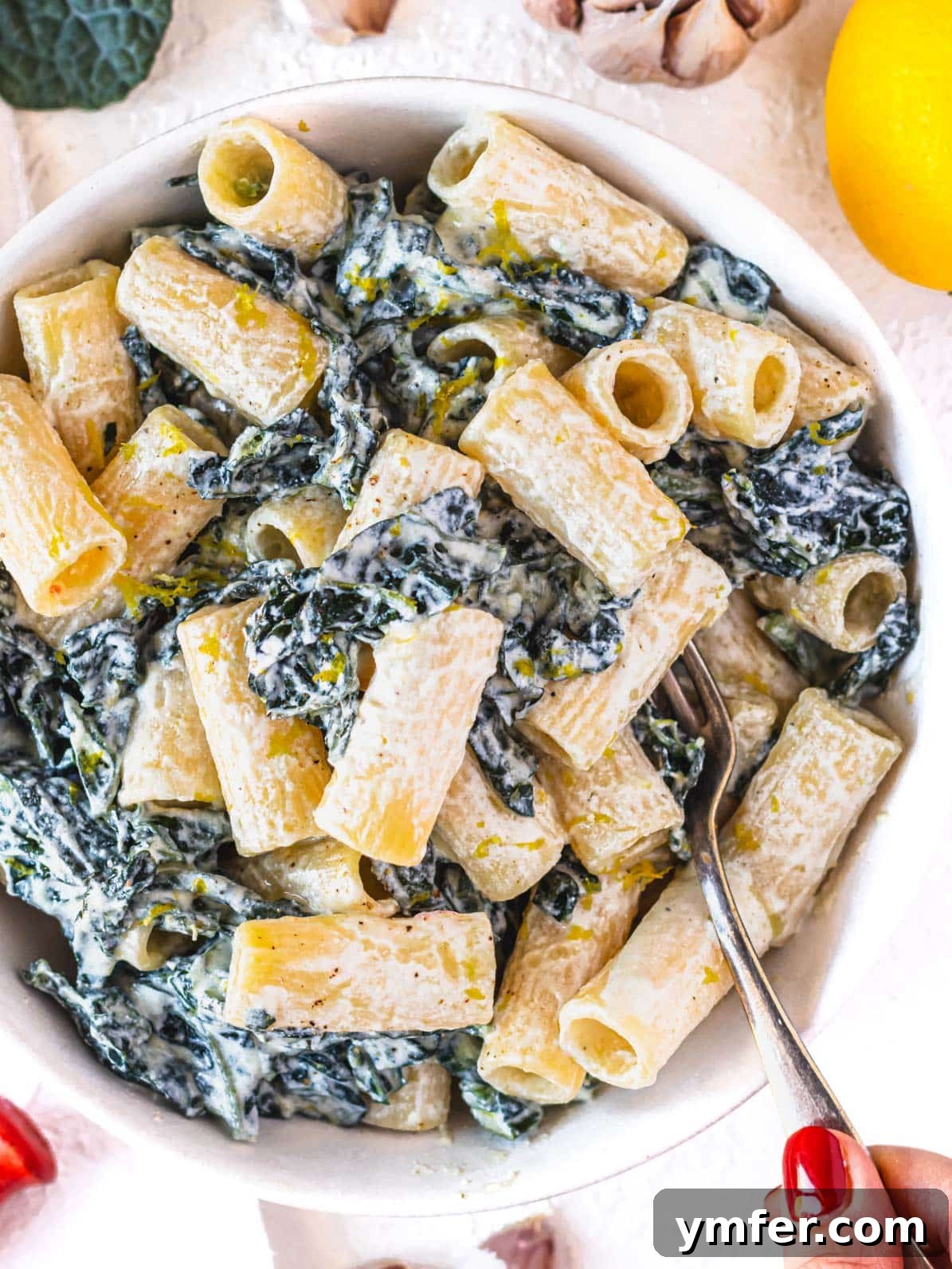 Royal Spire Sweet 2 A hand with red nail polish serving creamy kale pasta in a bowl
