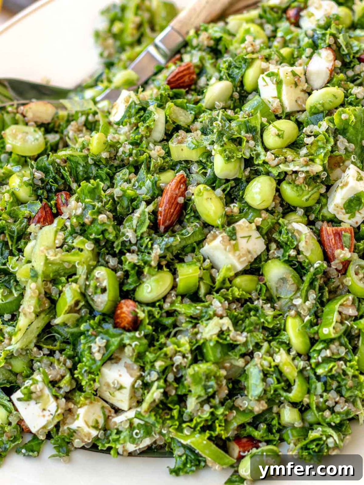 Close-up of kale quinoa salad in a white bowl, showing quinoa, kale, feta, edamame, almonds, and herbs tossed in lemon dressing