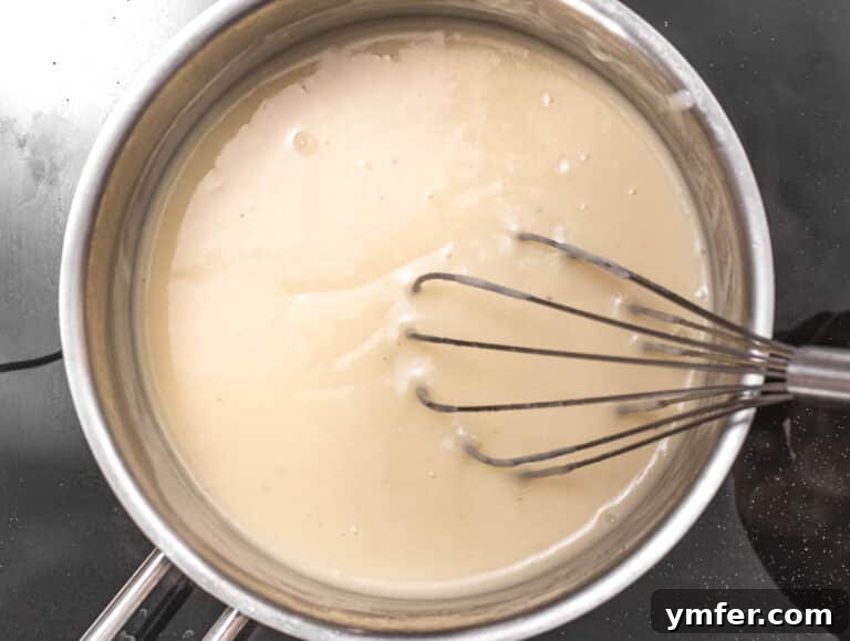 Luscious Vegan Cream Sauce 11 Vegan white sauce thickening beautifully in a pan, stirred with a whisk to ensure smoothness.